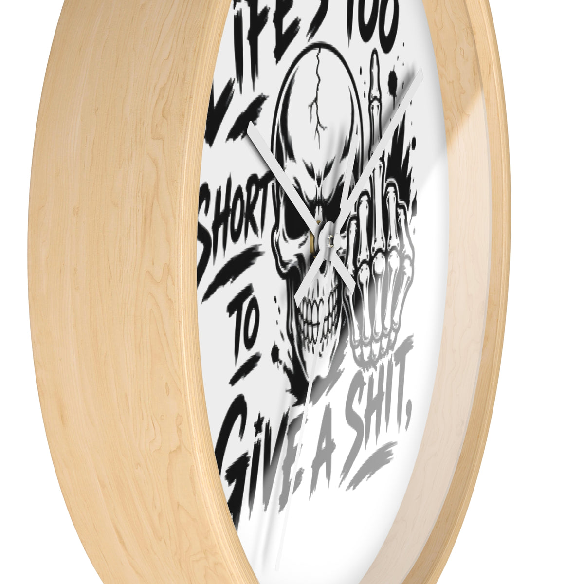 A close-up of a round wall clock with a light natural wood frame and a white face featuring a black skull graphic and bold text.