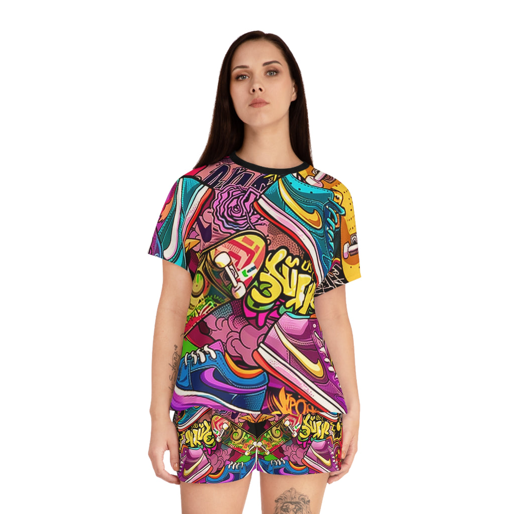 A woman modeling a matching short-sleeve t-shirt and shorts set with a vibrant, multicolor graffiti-style sneaker collage print, set against a plain white background.