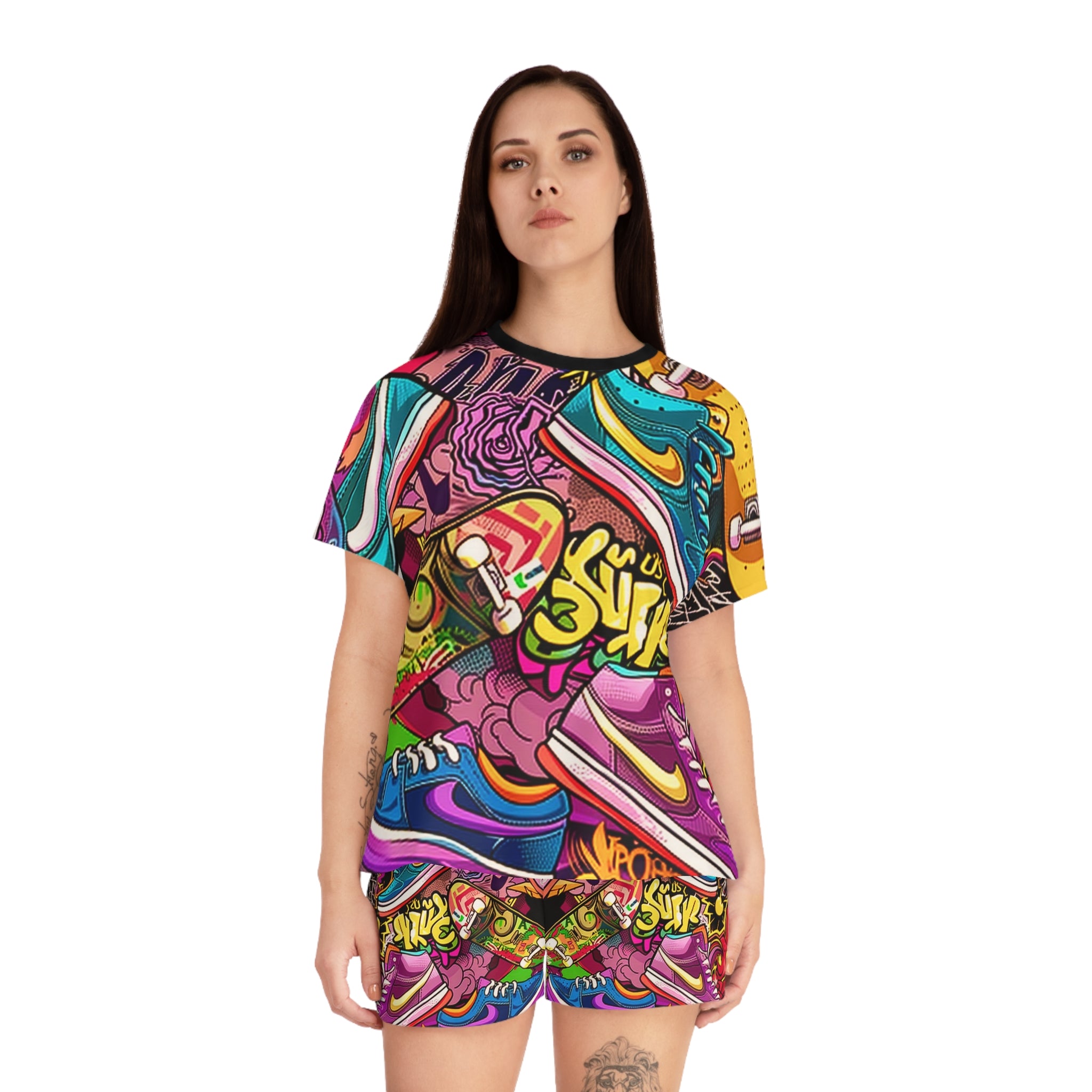 A woman modeling a matching short-sleeve t-shirt and shorts set with a vibrant, multicolor graffiti-style sneaker collage print, set against a plain white background.