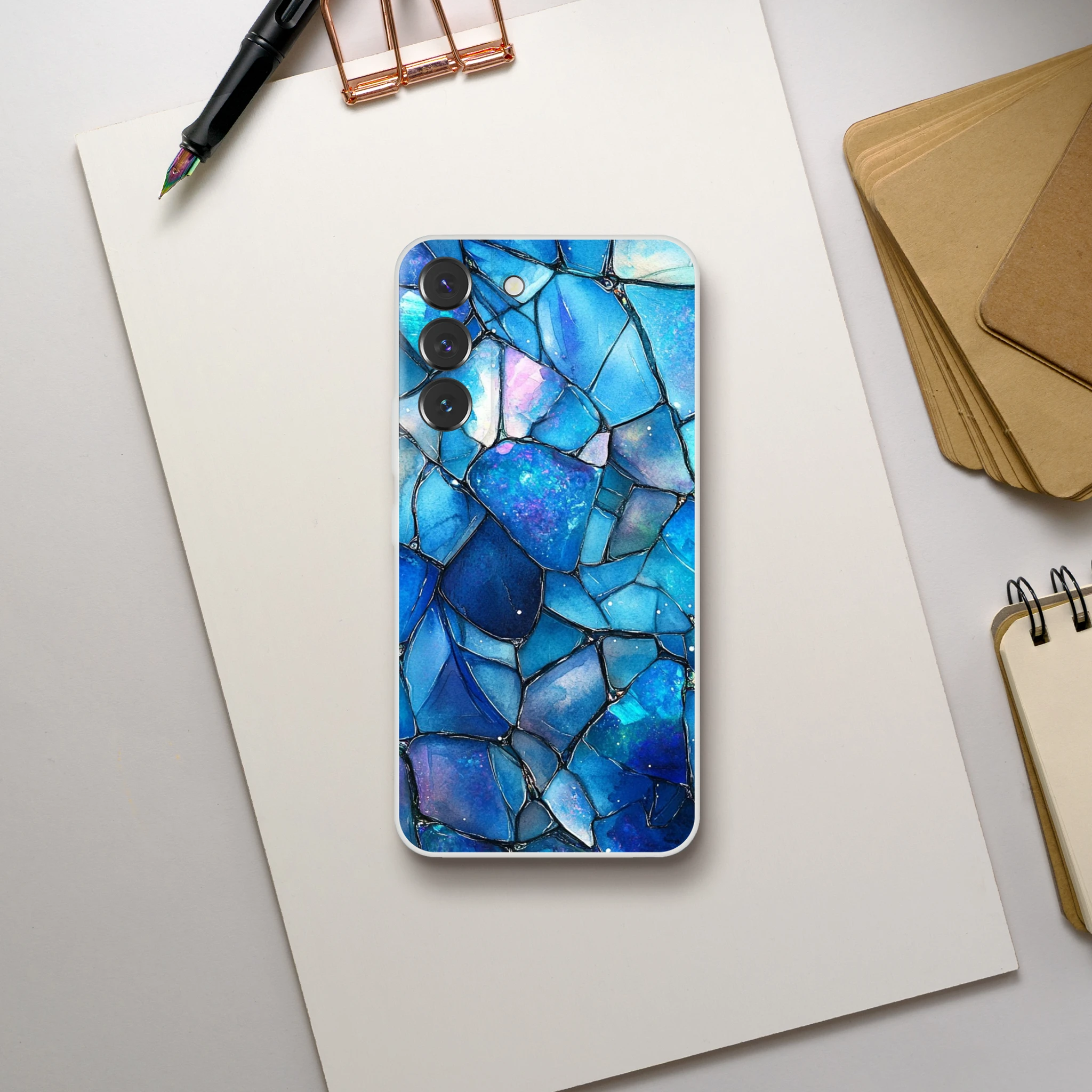 Phone case with blue mosaic design on a white surface with stationery items.