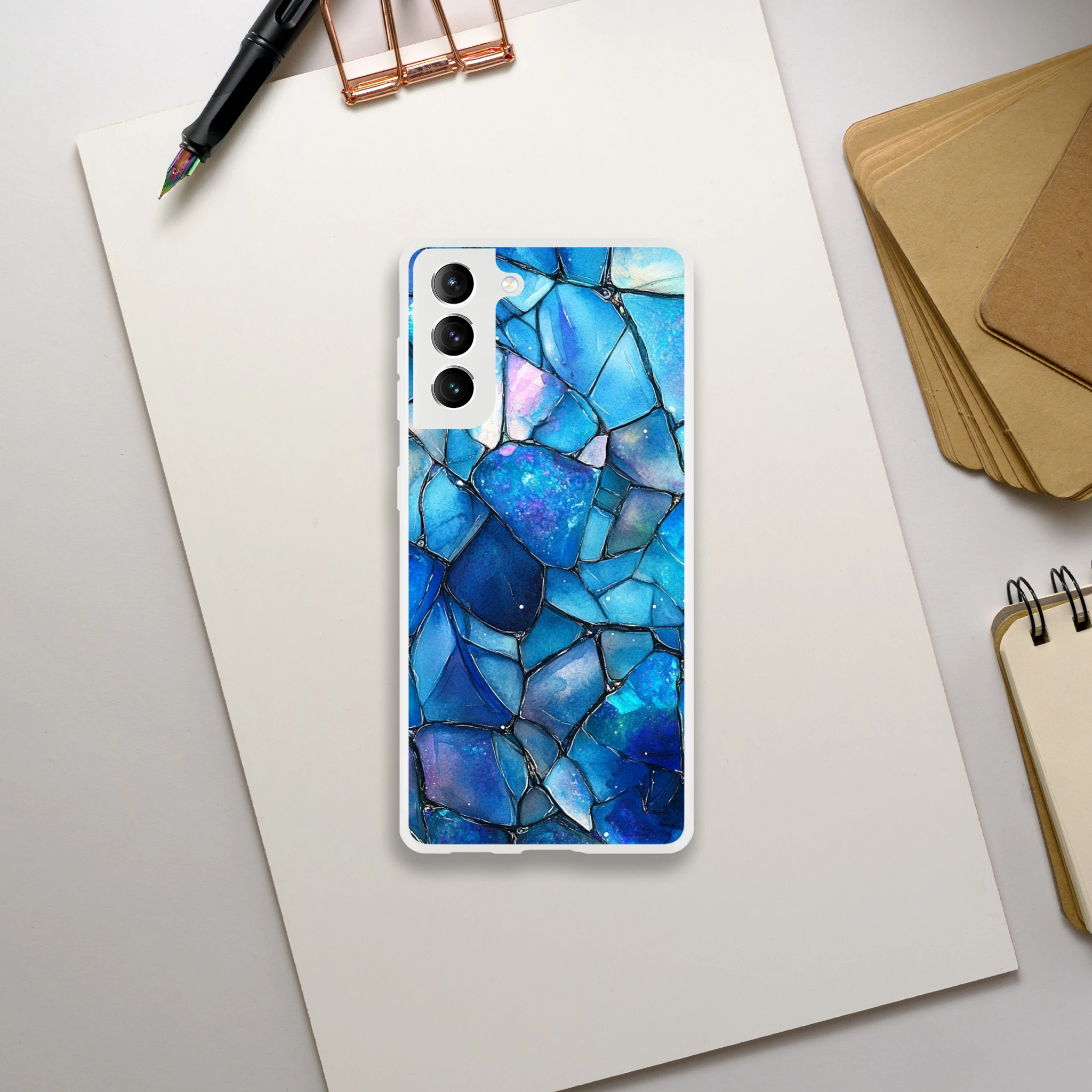 Phone case with blue mosaic design on a white surface with stationery items.