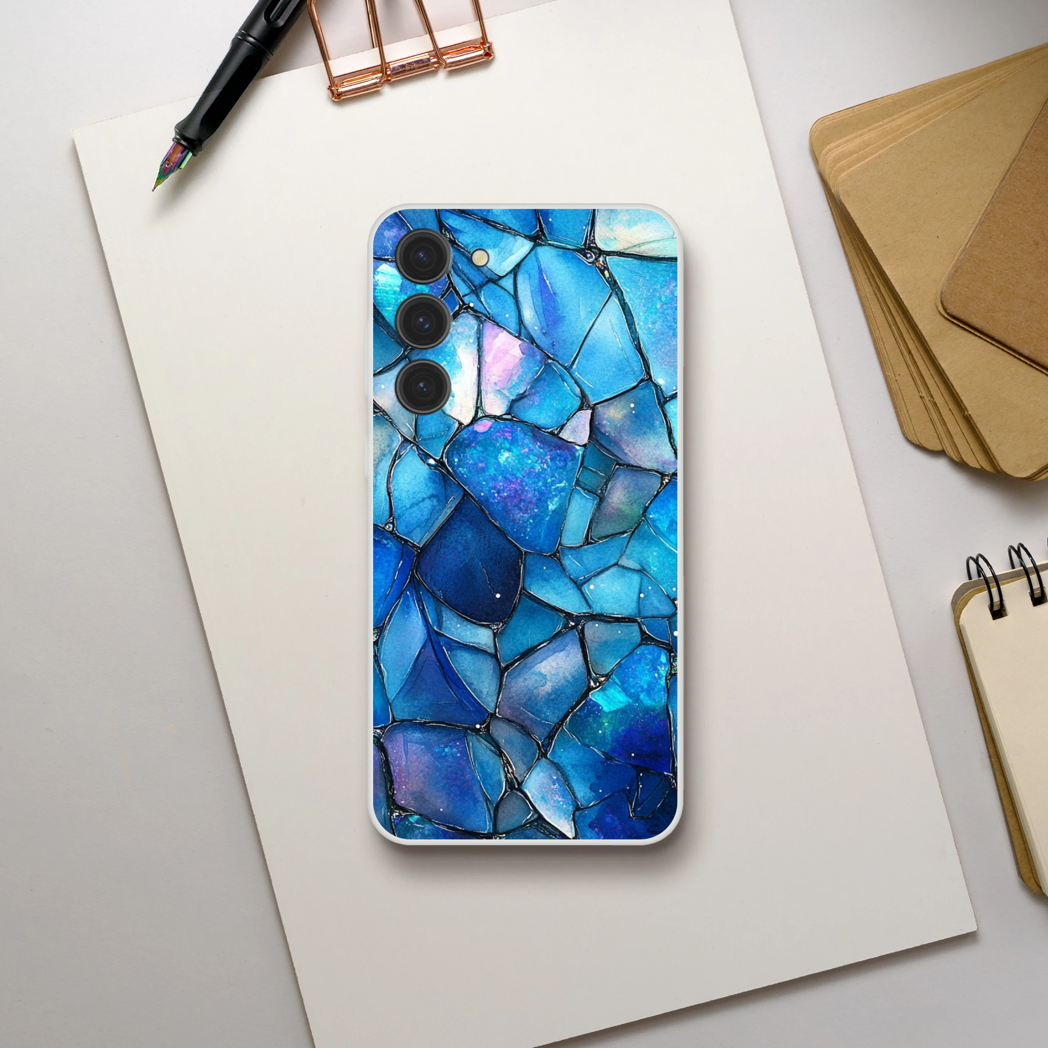 Phone case with blue mosaic design on a white surface with stationery items.