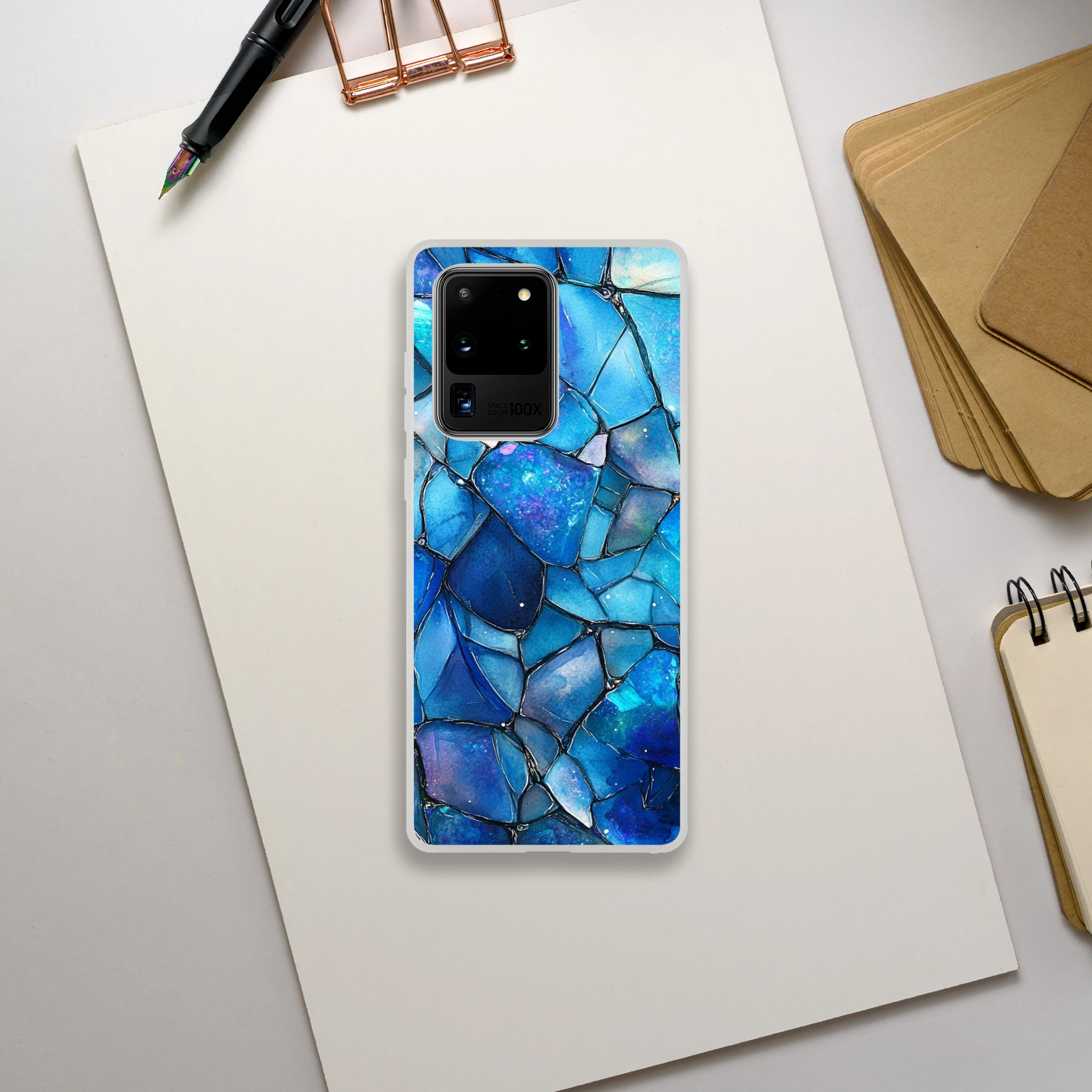 Phone case with blue mosaic design on a white surface with stationery items.