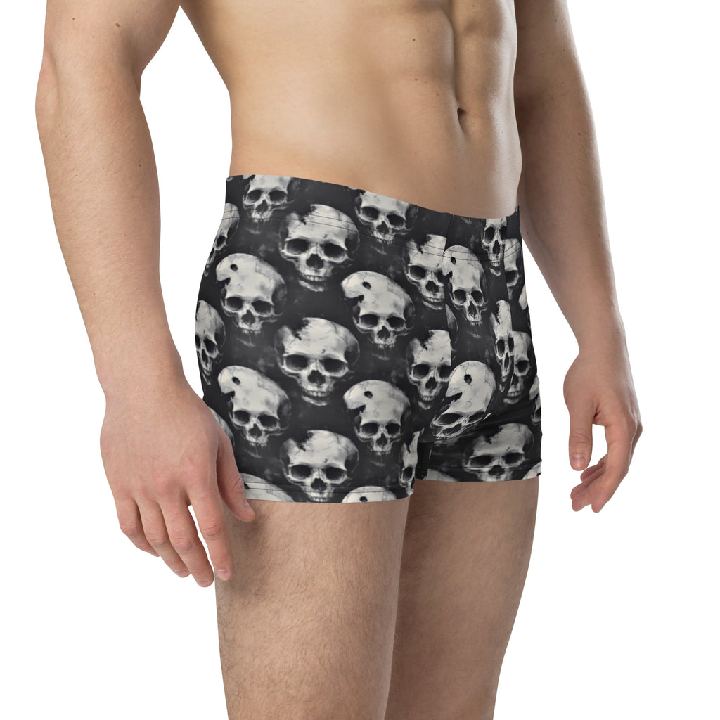A man wearing boxer briefs with an all-over skull print in white and gray on a black background, shown from the waist down against a plain white studio background.