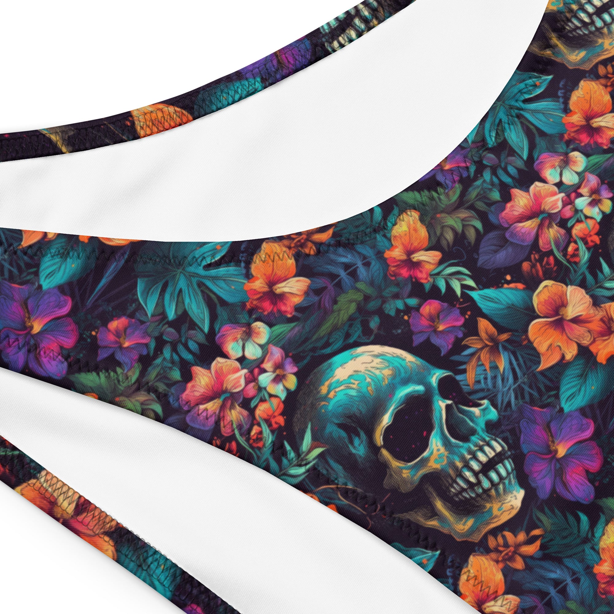 Close-up of a bikini top or swimsuit fabric with a dark tropical floral print featuring a large teal skull and colorful flowers, shown against a white background.