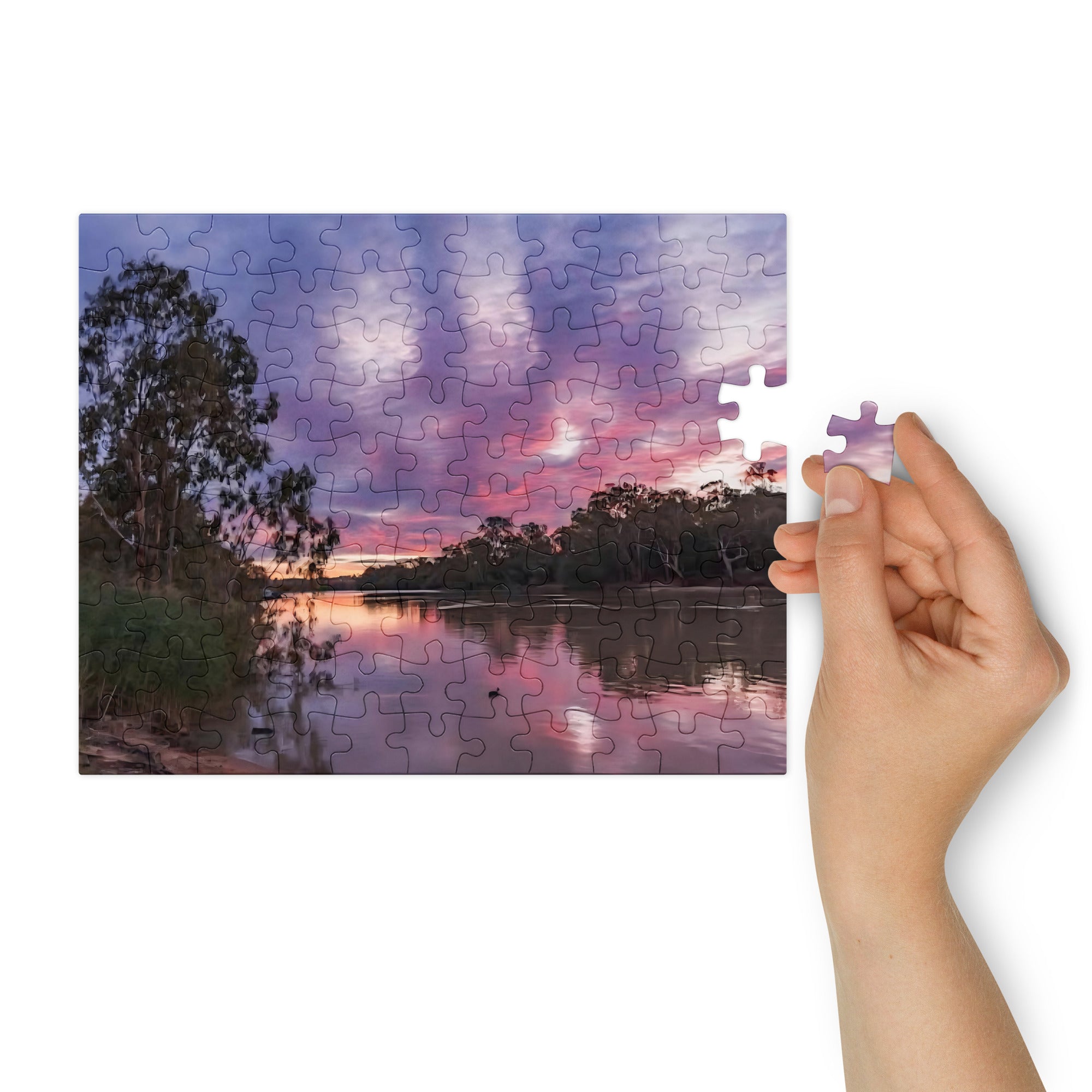Jigsaw puzzle with a sunset over a lake scene, held by a hand.