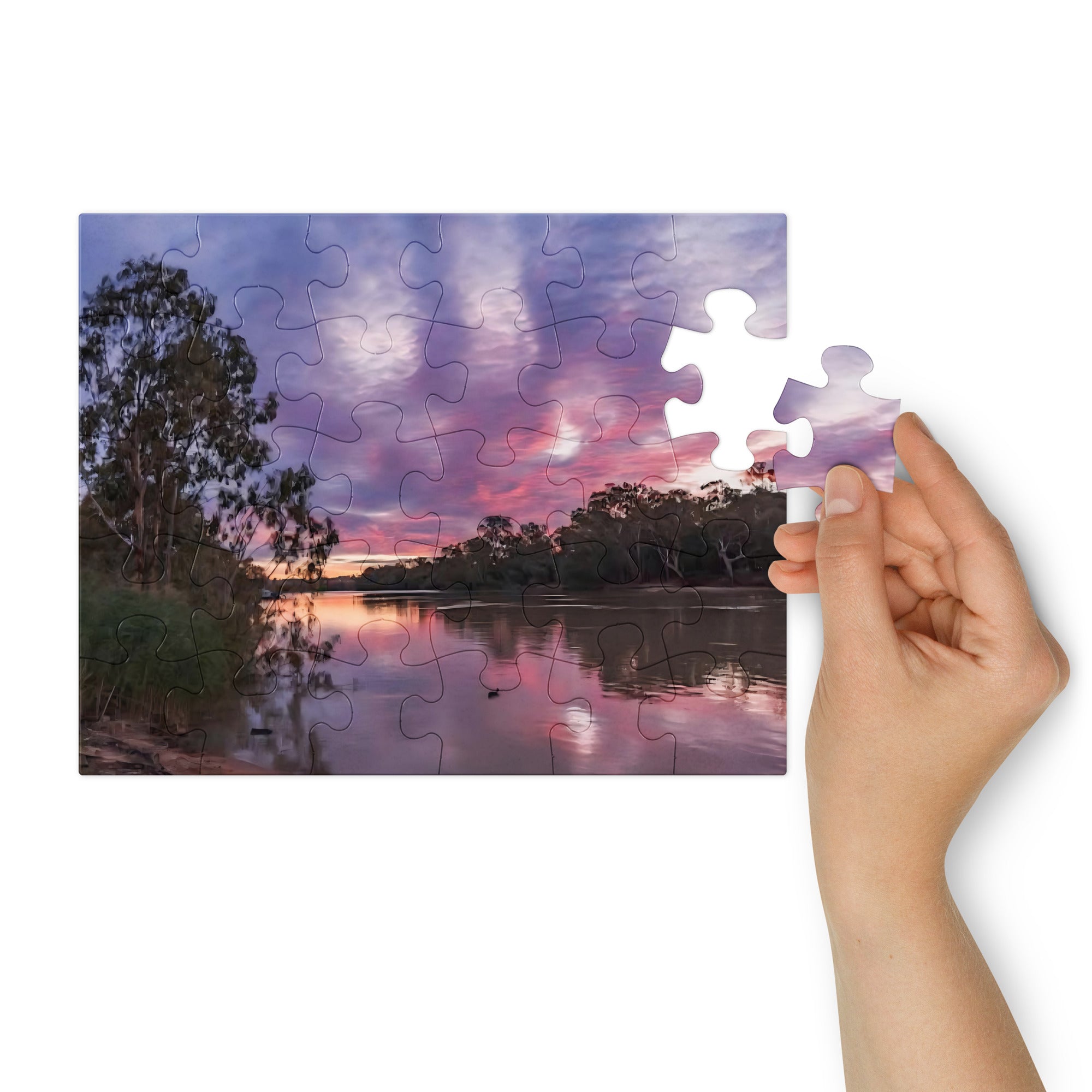 Jigsaw puzzle with a sunset over a lake scene, held together by a hand.