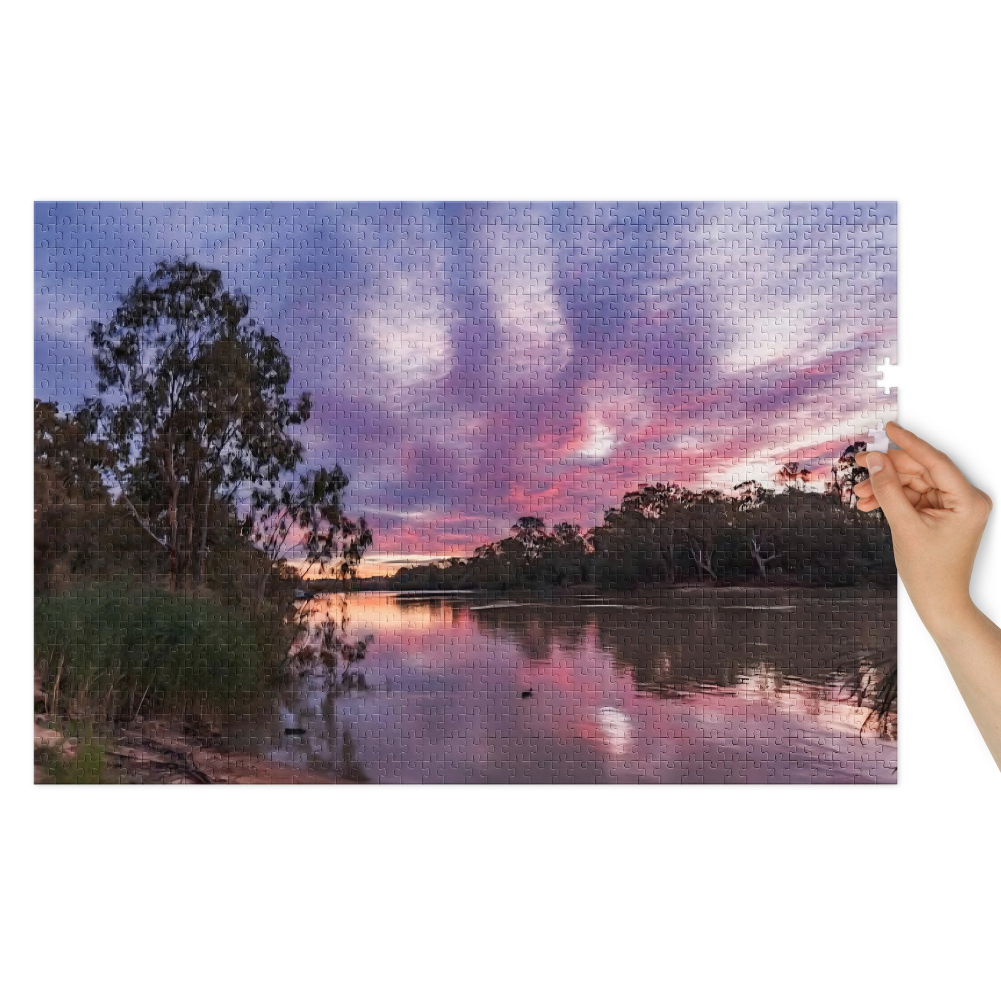 Hand holding a poster of a sunset over a lake with trees.